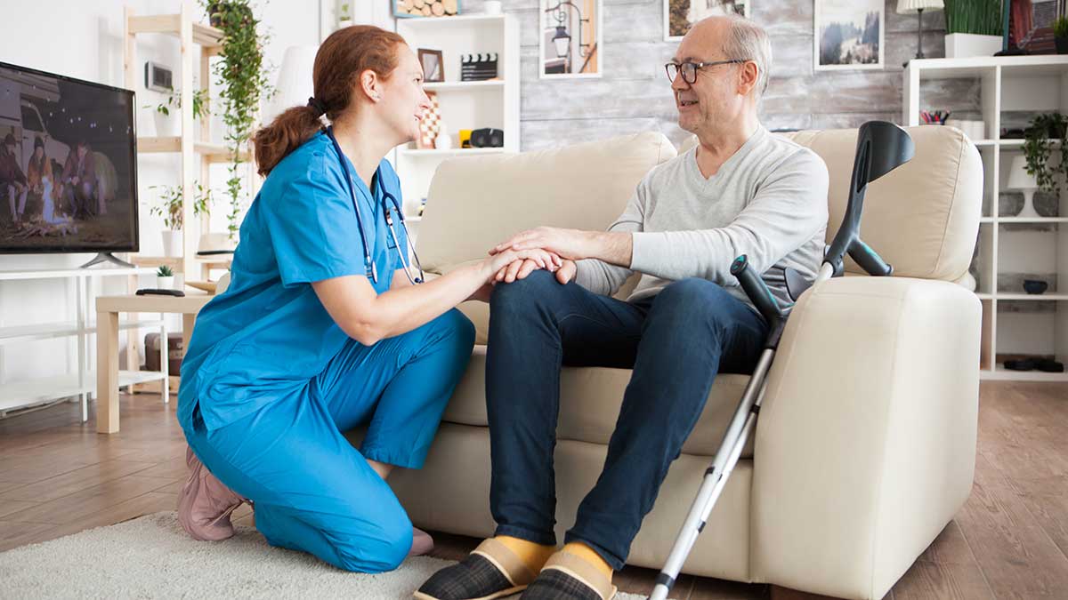 older man sitting on a couch talking to his Hospice nurse